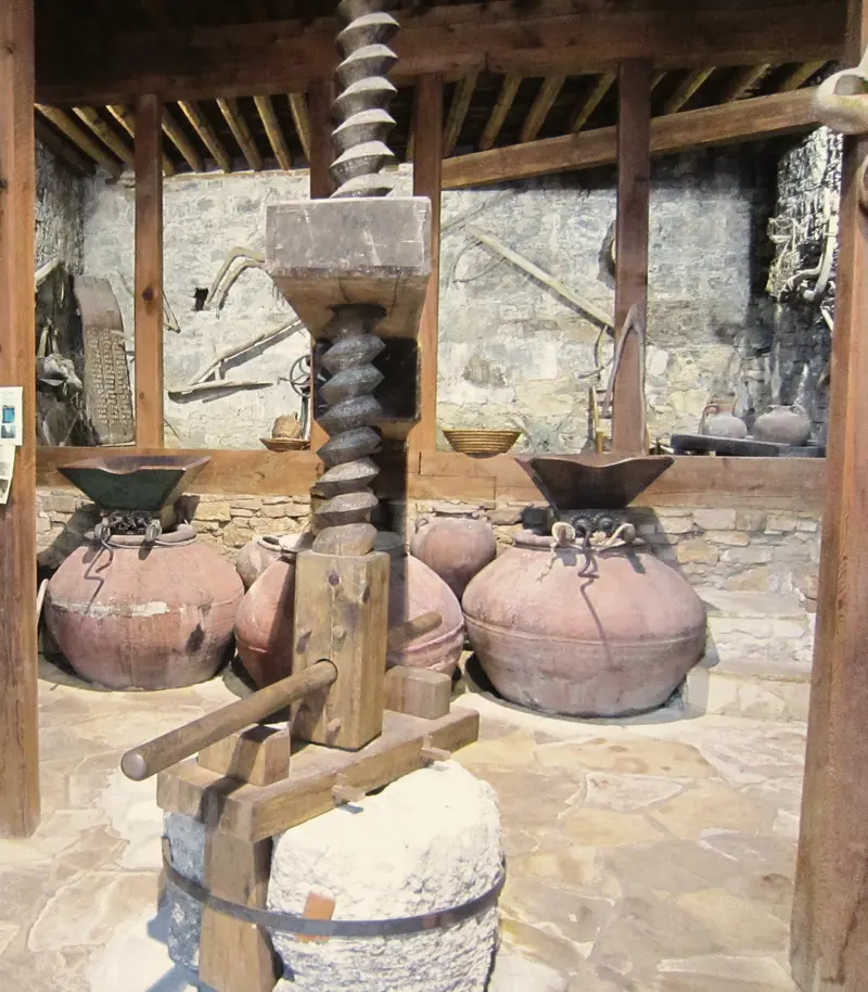 A huge wooden screw press and clay wine jars in an old stone press house