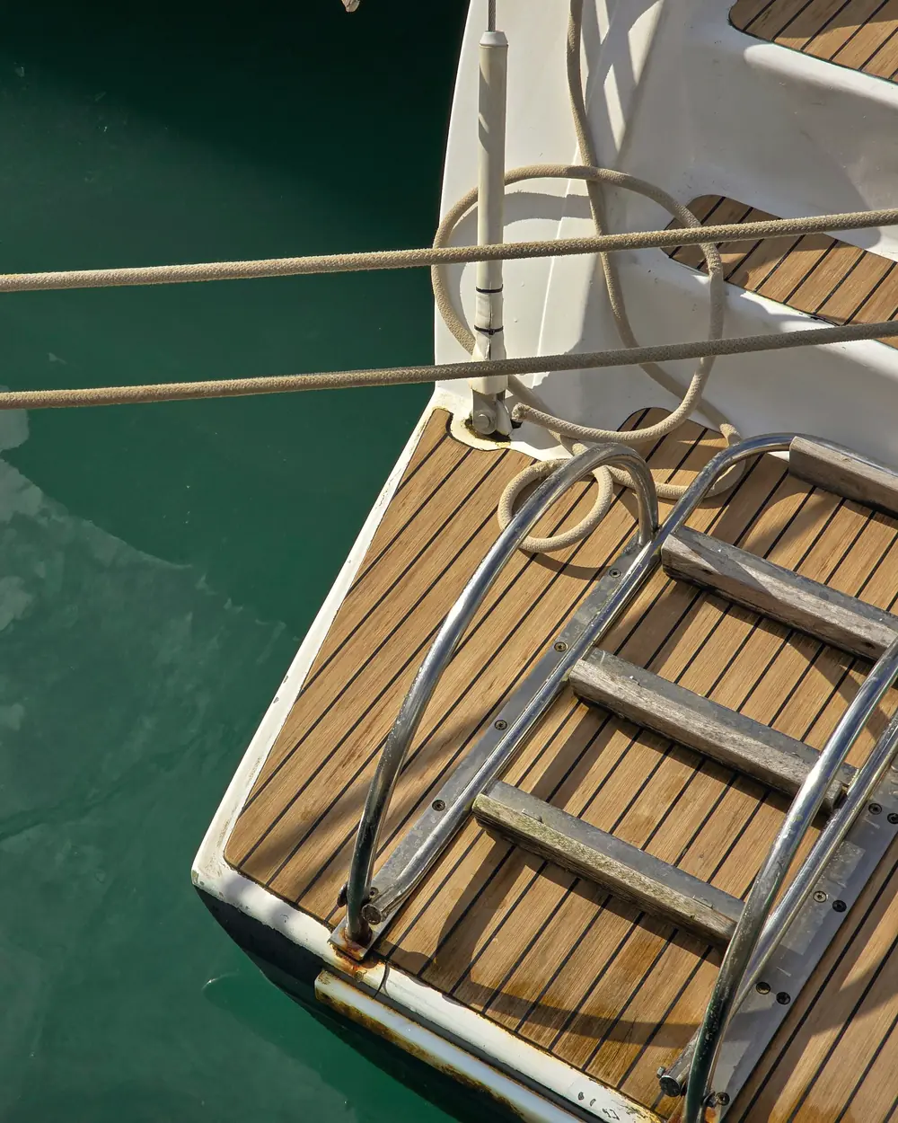 A teak swim platform and steel ladder down to green water