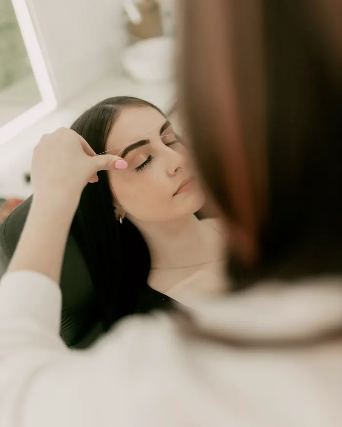 A client lying back with eyes closed while her brows are shaped