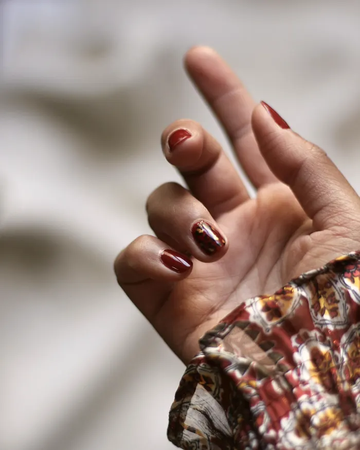 Short burgundy gel nails on a hand against a cream fabric