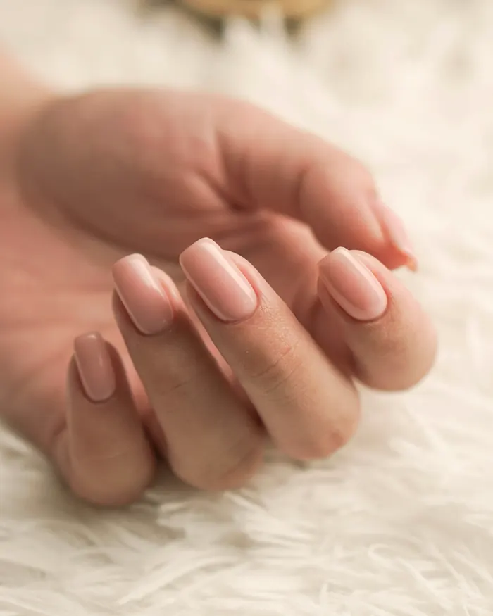 A relaxed hand with nude square nails resting on a soft white rug