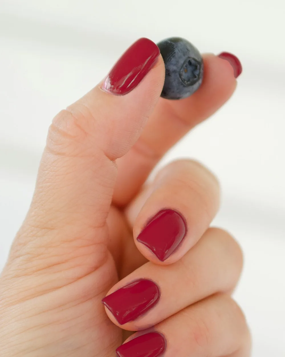 A hand holding a blueberry between two fingers, nails painted in the selected shade
