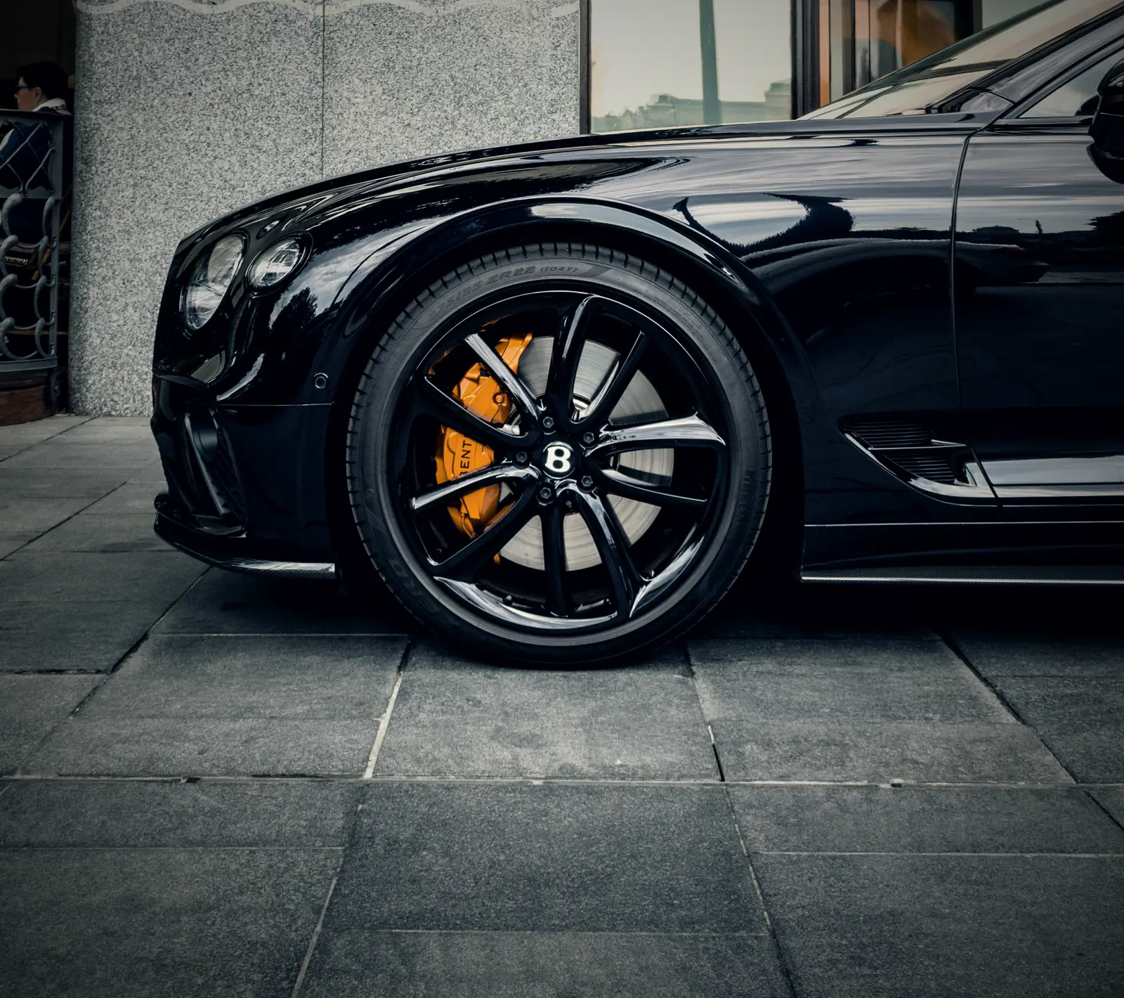 A black Bentley Continental GT with orange brake calipers parked on stone paving