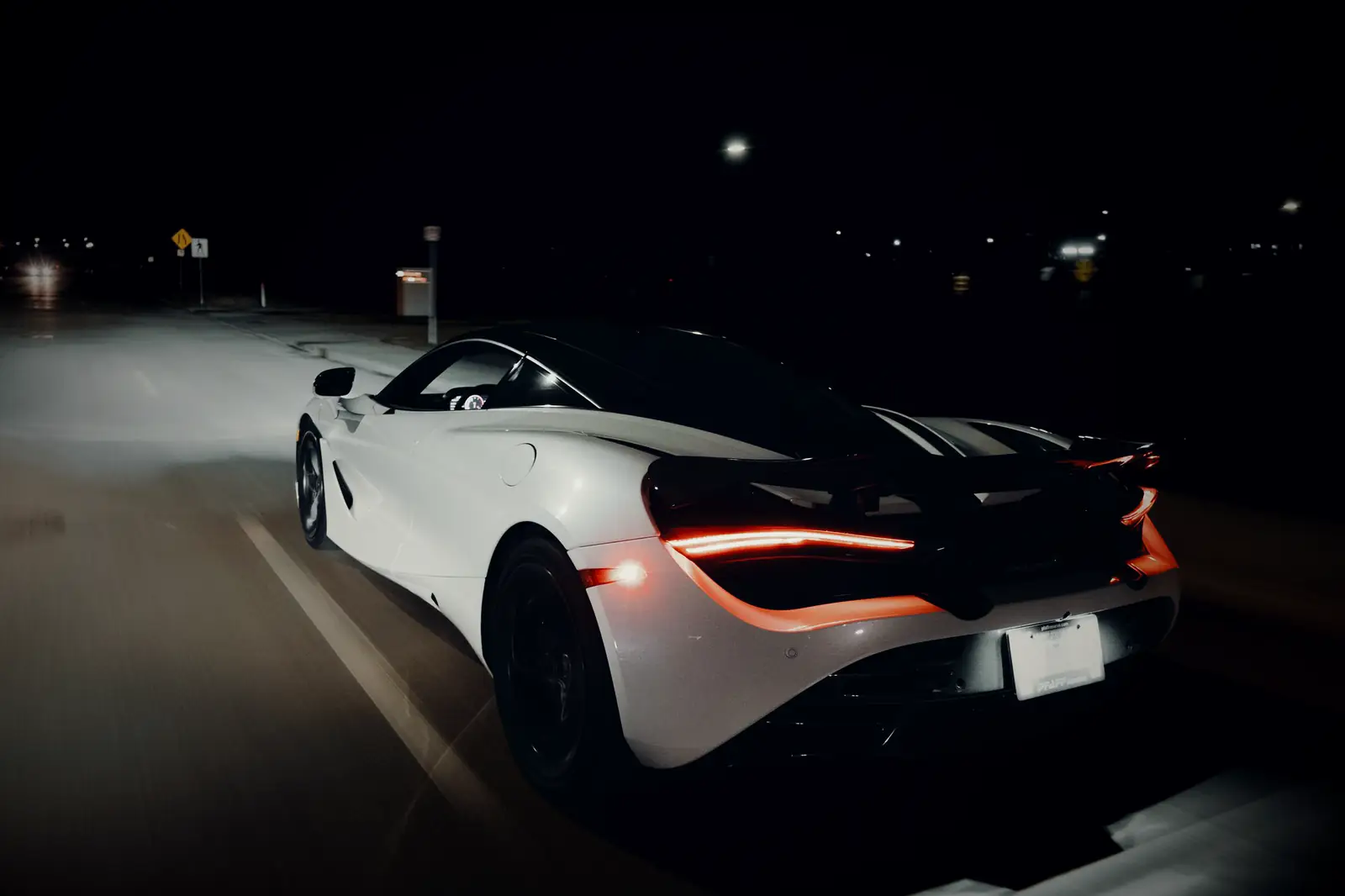 Rear of a white McLaren at night, tail lights glowing red
