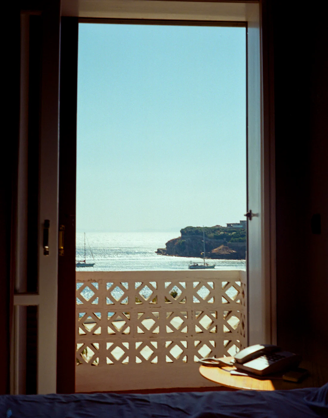 Open terrace doors framing the sea, boats and the far coastline
