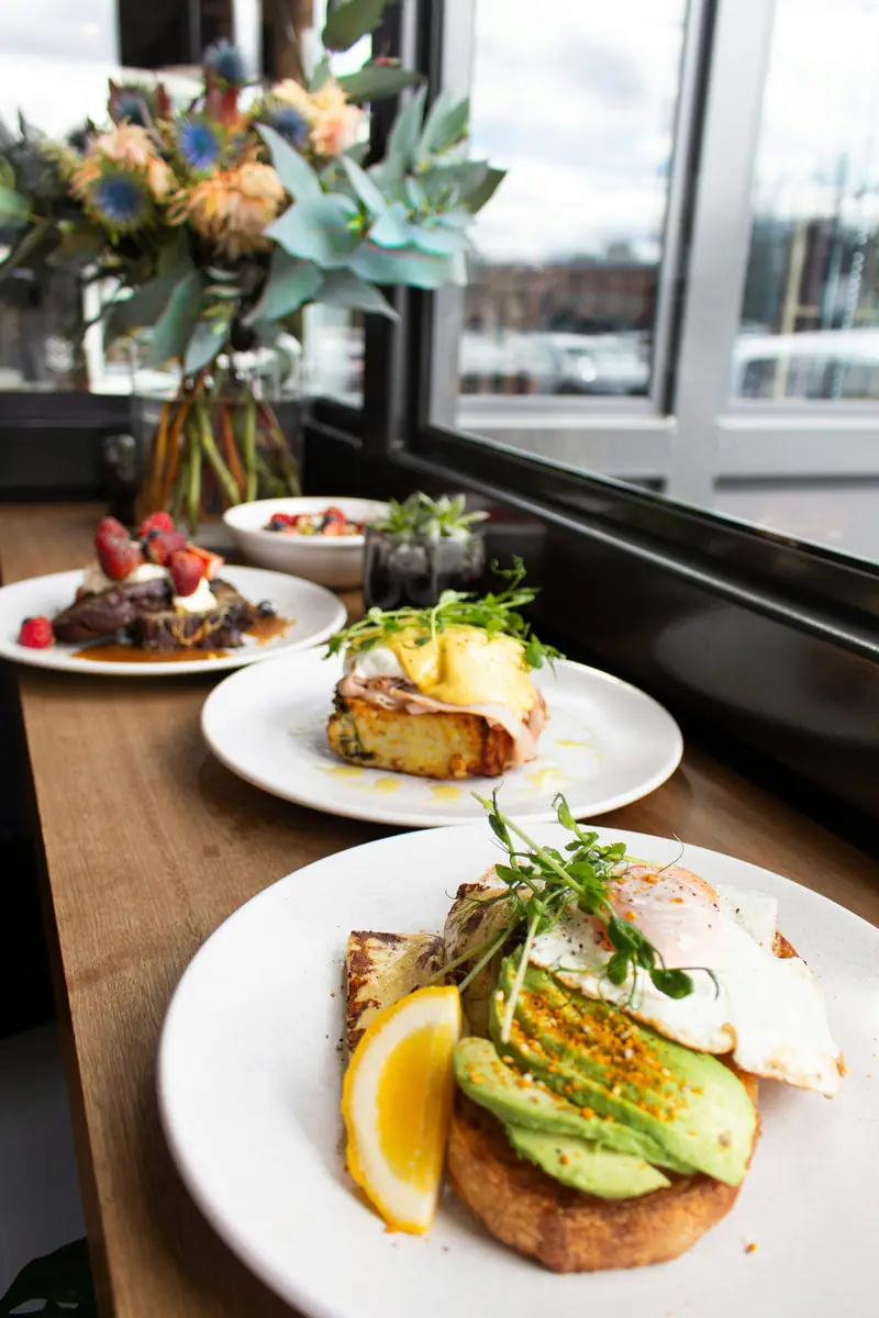 Window table set with eggs Benedict, avocado toast and French toast