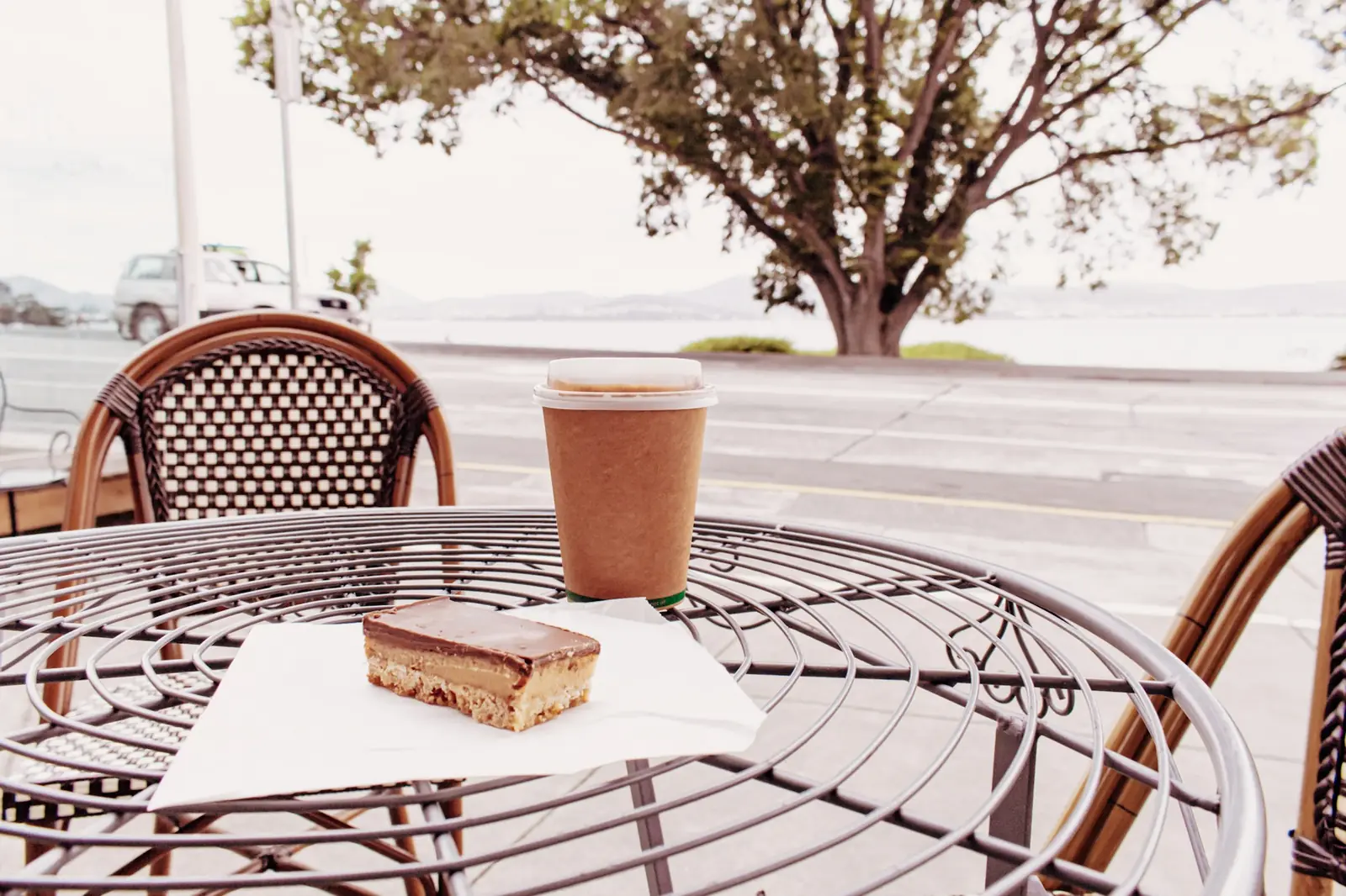 Terrace table with a coffee and a slice of cake, a tree and the sea behind