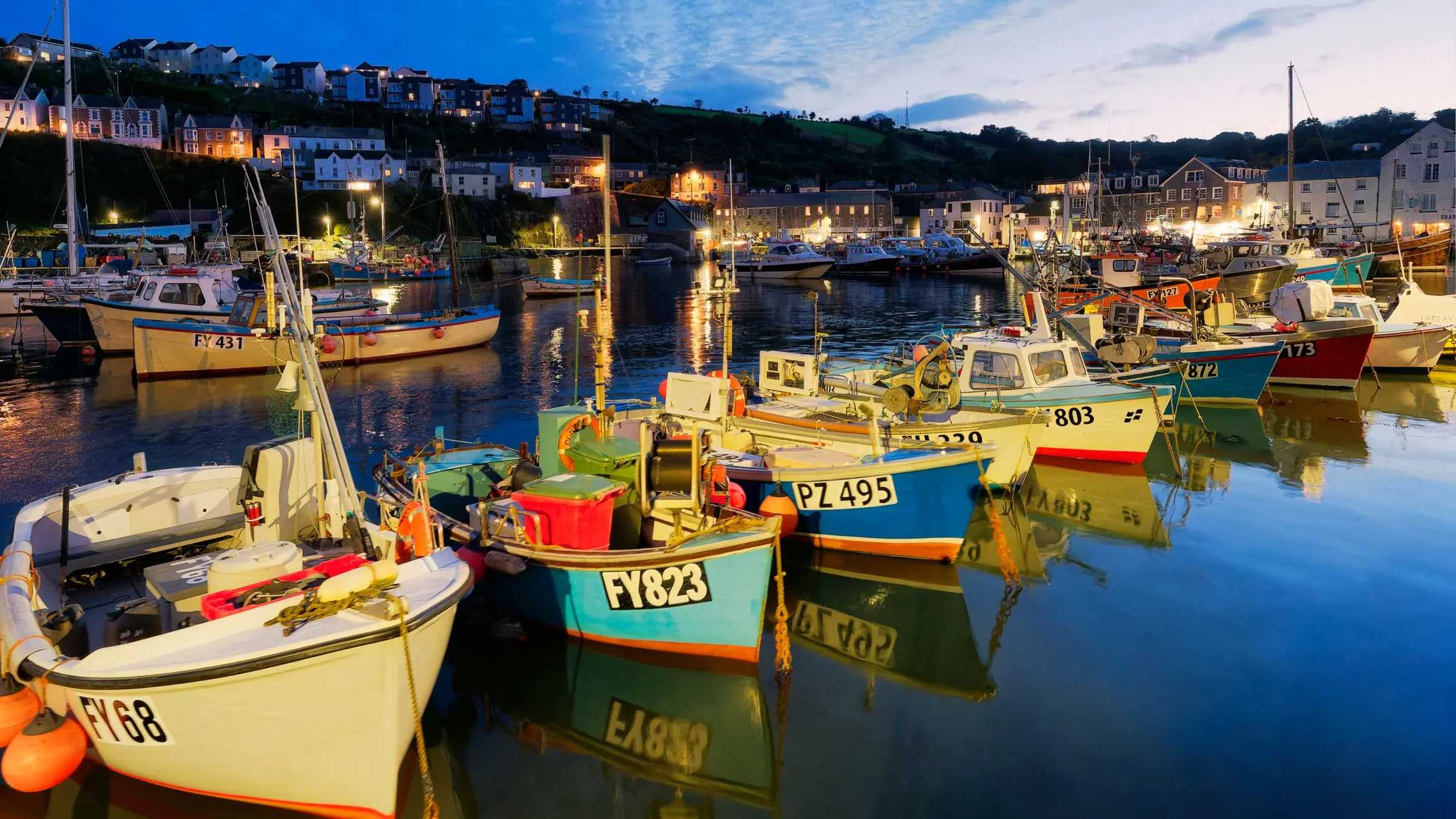 Fishing boats moored in a harbour at dusk, the town lights coming on